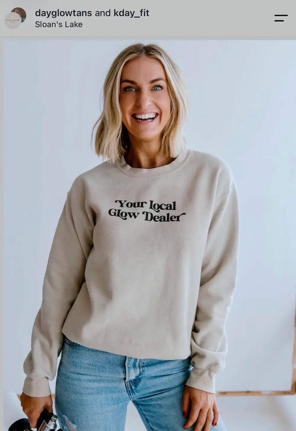 Spray tan artist wearing a Your Local Glow Dealer sweatshirt